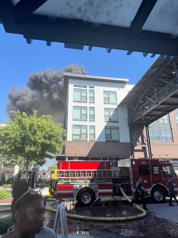 Smoke billows from an apartment building while a fire truck sits in front of it.
