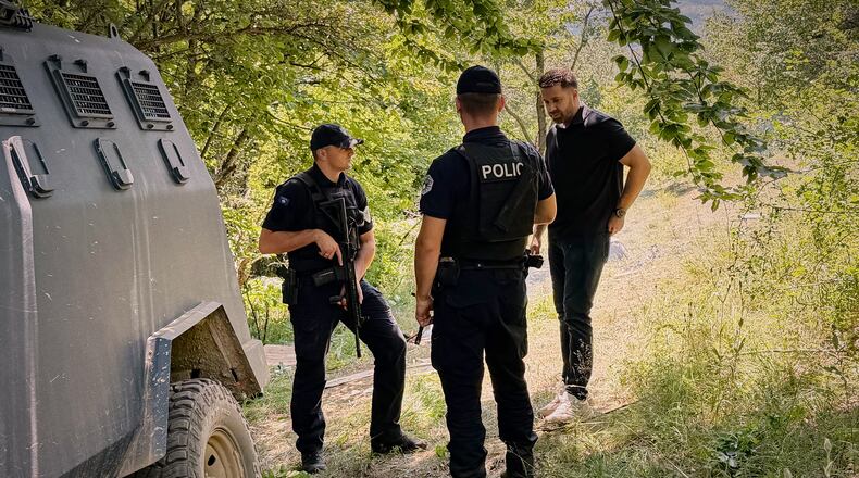 Erblin Ademi, right, whose father, Adem Ademi, a prominent surgeon, disappeared along with 22 other intellectuals during the Kosovo war in April 1999, speaks to police officers near the excavation site of a mass grave in Small Kalluder, Kosovo, Wednesday, Aug. 5, 2026. (AP Photo/Zana Cimili)