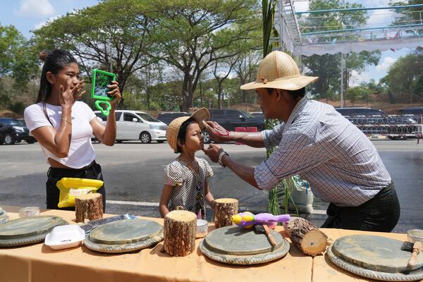 A man applies Thanakha, traditional make-up, on his child’s face as they take part in the first day of annual water festival also known as "Thingyan," in Naypyitaw, Myanmar, Sunday, April 13, 2025. (AP Photo/Aung Shine Oo)