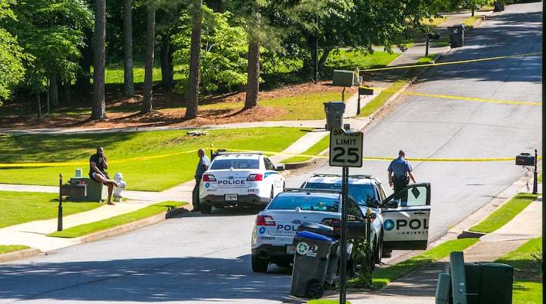 A witness (seated left) talks with Gwinnett County police after a shooting on Highland Gate Circle on Monday morning. According to police, a woman opened fire on a school bus as it was leaving a bus stop.
