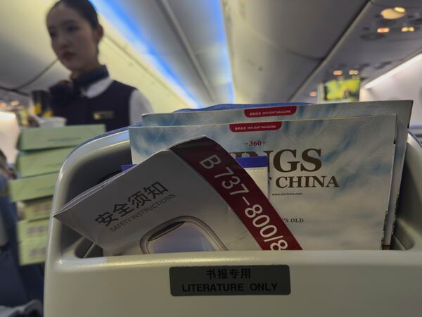 A stewardess walks by a seat compartment displaying a safety instruction leaflet of an Air China airlines Boeing 737-800 together with magazines on a seat compartment during a flight in China, Wednesday, April 16, 2025. (AP Photo/Andy Wong)