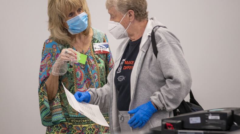In May, a poll worker in Lawrencevill Rae Gilmer (left) wears a face mask and gloves as she assist a voter during early voting. Sandy Springs approved a resolution July 12 in support of wearing face coverings. (ALYSSA POINTER / ALYSSA.POINTER@AJC.COM)