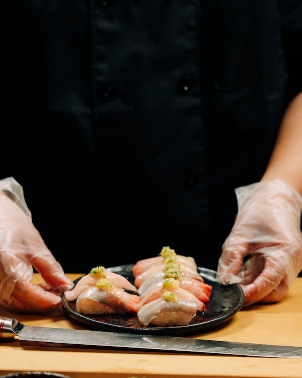 A plate of nigiri held by two hands in plastic gloves at 1678 Omakase.