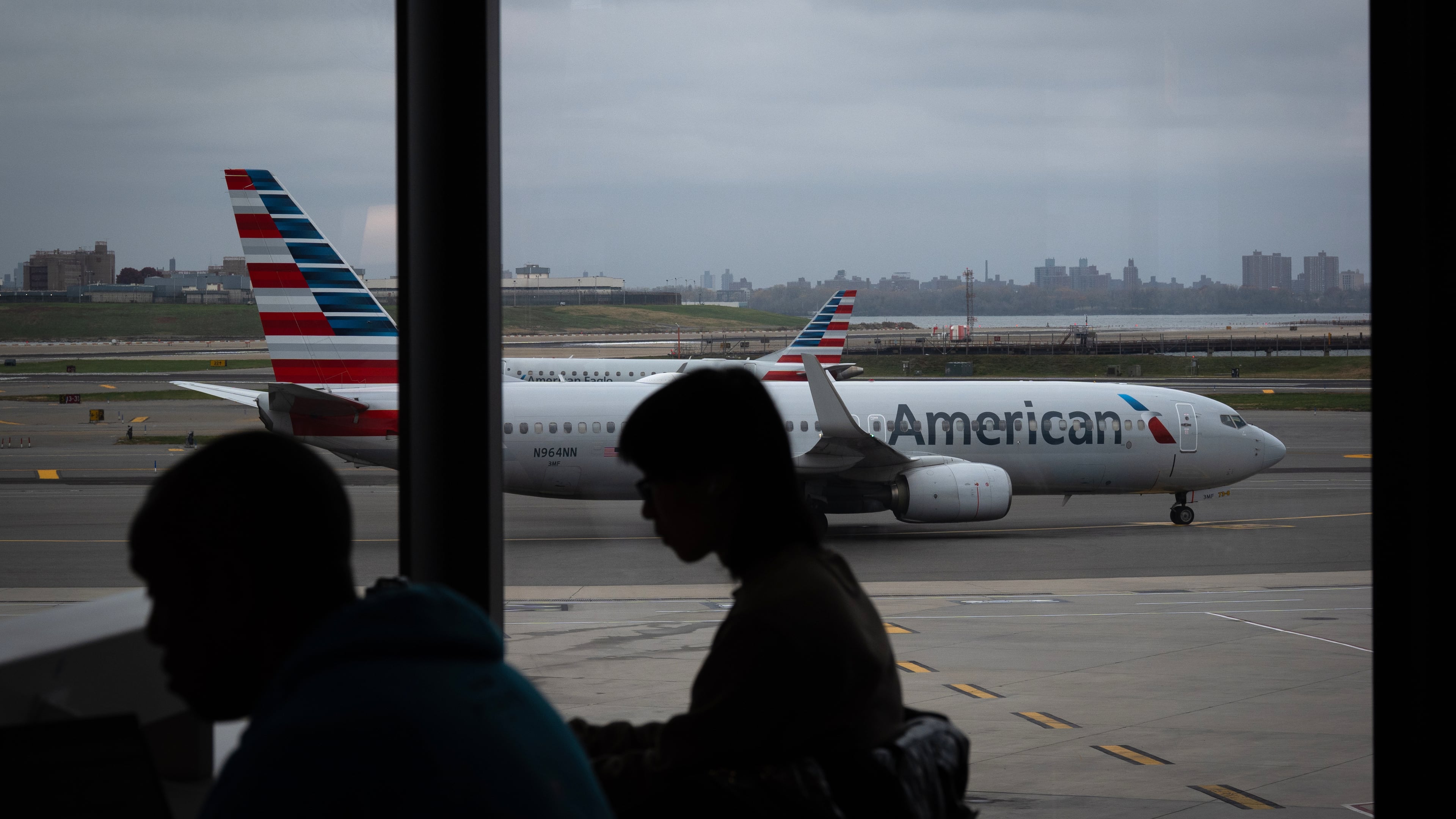 People wait for flights as an American Airlines plane taxis at LaGuardia Airport (LGA), in the Queens borough of New York, Sunday, Nov. 9, 2025. (AP Photo/Adam Gray)