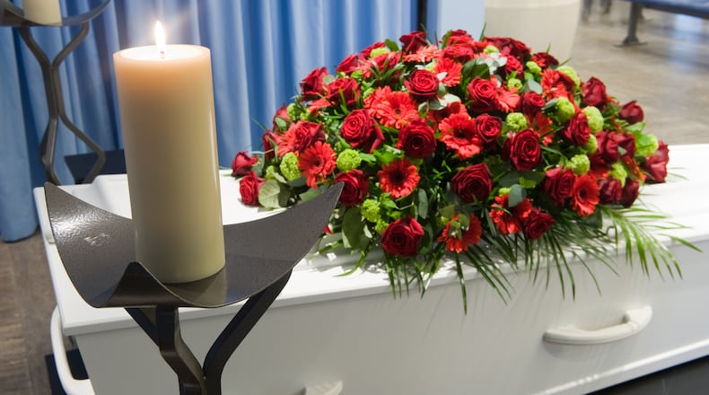 A coffin with a flower arrangement in a morgue and a burning candle in front