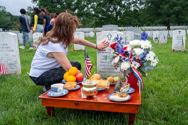FILE - Kim Hoan Nguyen, of Falls Church, Va., who is originally from Vietnam, touches her son's gravestone next to ritual offerings in the Vietnamese tradition at the gravesite of her son, Marine Corporal Binh N Le, who died serving in Iraq in 2004, in Section 60 of Arlington National Cemetery, in Arlington, Va., Monday, May 27, 2024, on Memorial Day. (AP Photo/Jacquelyn Martin, File)
