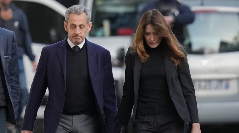 Former French President Nicolas Sarkozy and his wife Carla Bruni-Sarkozy leave their home Tuesday, Oct. 21, 2025 in Paris as Nicolas Sarkozy heads to prison to serve time for a criminal conspiracy to finance his 2007 election campaign with funds from Libya. (AP Photo/Thibault Camus)