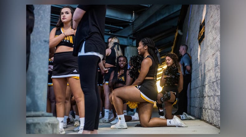 Three cheerleaders are seen kneeling in the tunnel by the field during the national anthem before Saturday's matchup between Kennesaw State and Gardner-Webb, Saturday, Oct. 21, 2017. Four cheerleaders kneeled during the anthem to continue the protests at KSU football games.
