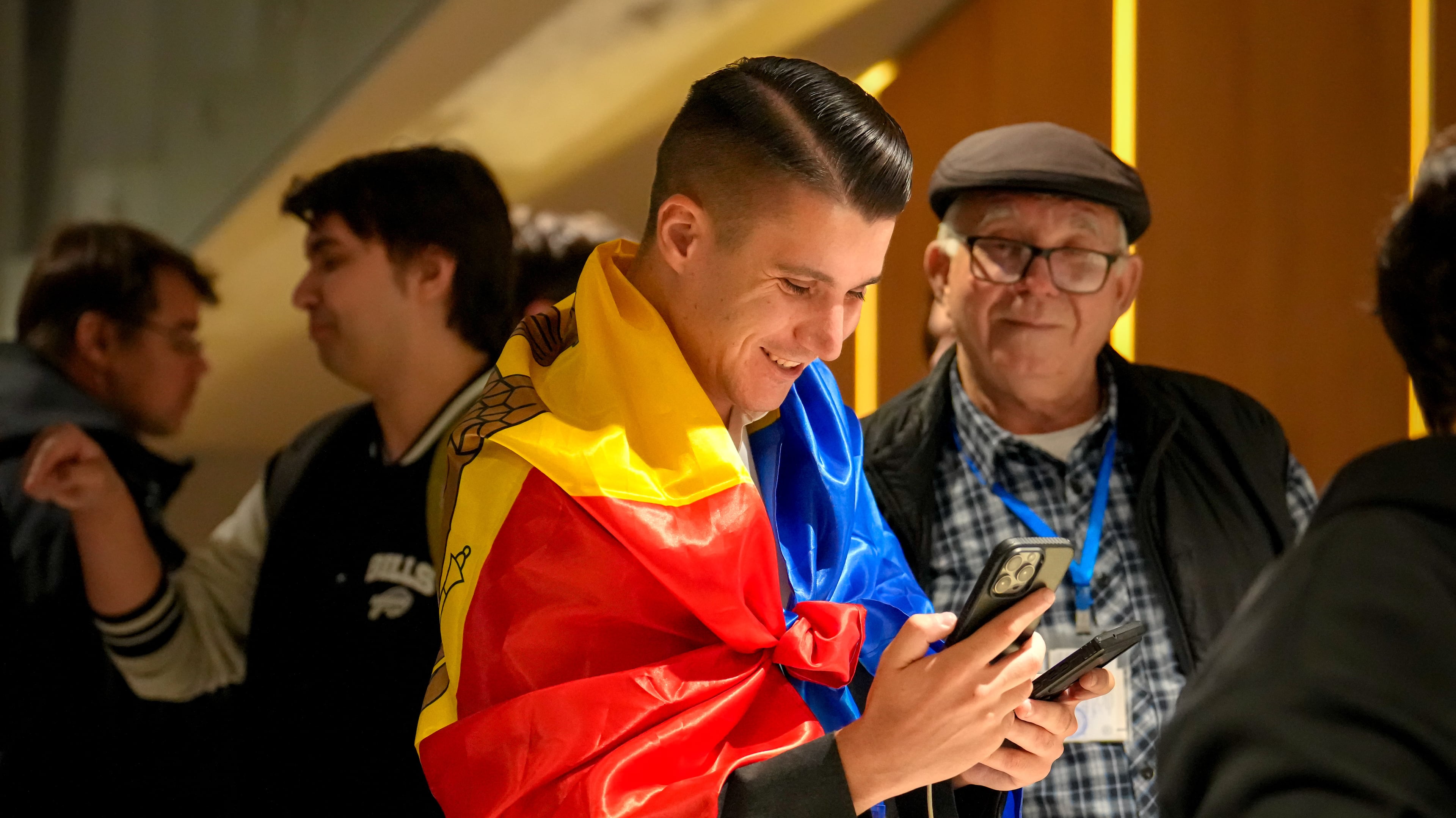 A supporter of the pro-EU Party of Action and Solidarity (PAS) draped in the Moldovan flag smiles as he checks partial results on a phone after the polls closed for the parliamentary election, in Chisinau, Moldova, Sunday, Sept. 28, 2025. (AP Photo/Vadim Ghirda)