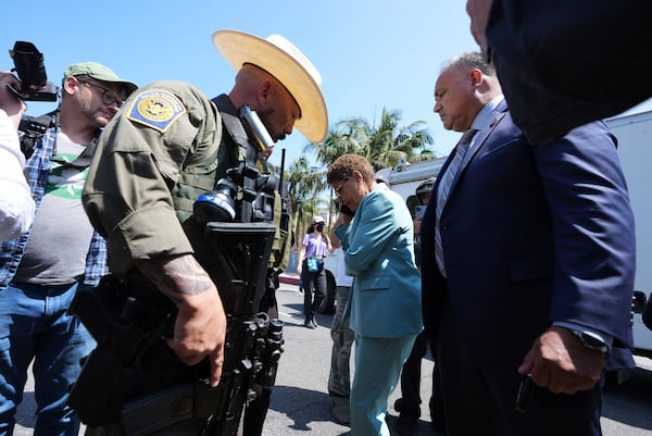 Los Angeles Mayor Karen Bass talks on her mobile phone next to a border patrol federal agent at MacArthur Park Monday, July 7, 2025, in Los Angeles. (AP Photo/Damian Dovarganes)