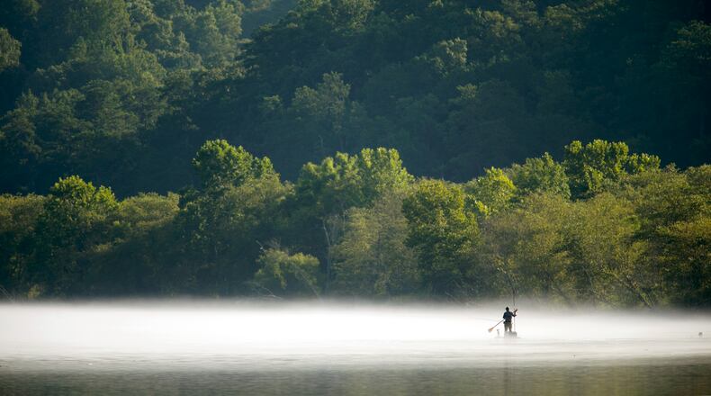 A fisherman paddles through the fog on a paddle board to fish on the Chattahoochee River at Morgan Falls Overlook Park Sunday, July 19, 2015.