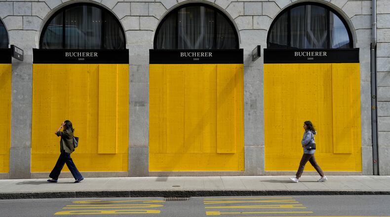 Pedestrians walk past the boarded-up windows of a shop, ahead of expected protests for the G7 summit, in Geneva, Switzerland, Tuesday, June 9, 2026. (AP Photo/Baz Ratner)