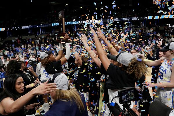 UCLA players celebrate with the trophy after their win against LSU in the Elite Eight of the NCAA college basketball tournament, Sunday, March 30, 2025, in Spokane, Wash. (AP Photo/Young Kwak)