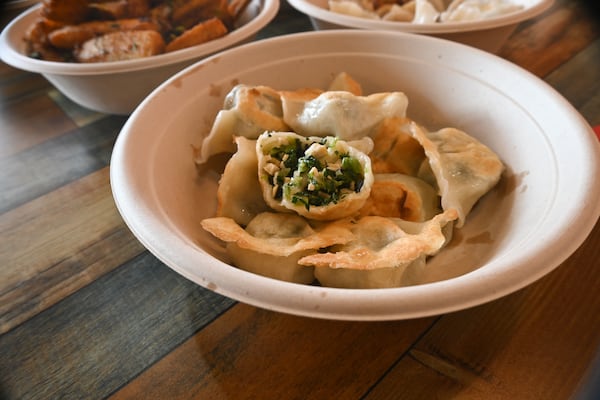 Pan-fried veggie dumplings in a bowl, one cut open to reveal it filled with tofu skin, chives and wood ear mushrooms.