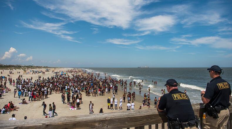 Police officers watch a crowd of partiers gather on the beach for Orange Crush Saturday afternoon at Tybee Island. Police are investigating several incidents, including the attack of two women Sunday at the beach.
