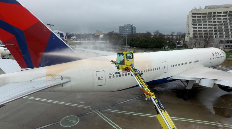 A worker sprays a de-icing solution on a Delta Air Lines jet in this February file photo. RYON HORNE/RHORNE@AJC.COM