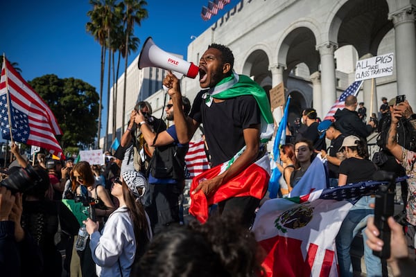 A man shouts into a megaphone outside City Hall during protests over federal immigration enforcement raids on Wednesday, June 11, 2025, in Los Angeles. (AP Photo/Ethan Swope)