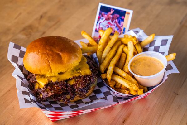 A paper boat at a restaurant with a double-patty smashburger with american cheese and a side of fries with dipping sauce.