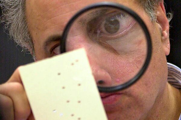FILE - Broward County, Fla. canvassing board member Judge Robert Rosenberg uses a magnifying glass to examine a disputed ballot at the Broward County Courthouse in Fort Lauderdale, Fla., Nov. 24, 2000. (AP Photo/Alan Diaz, File)