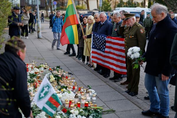 People with U.S. national flag come to pay their last respect to the three soldiers found dead on Monday at a training range in Pabrade, near the U.S. Embassy in Vilnius, Lithuania, Tuesday, April 1, 2025. (AP Photo/Mindaugas Kulbis)