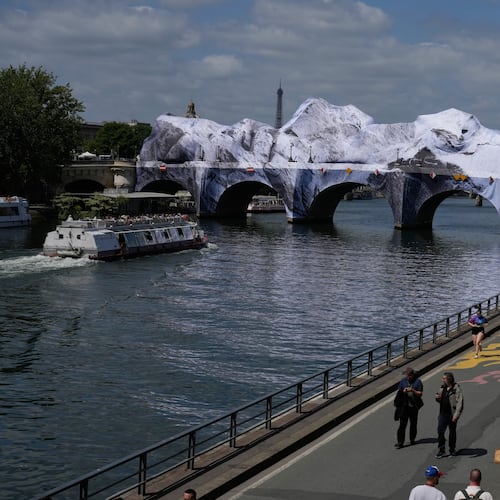 People walk along the Seine river next to "The Pont Neuf Cave," an inflated art installation by French street artist JR, on Paris' oldest bridge, the Pont Neuf, Thursday, May 21, 2026, which will be open to the public from June 6-28. (AP Photo/Michel Euler)