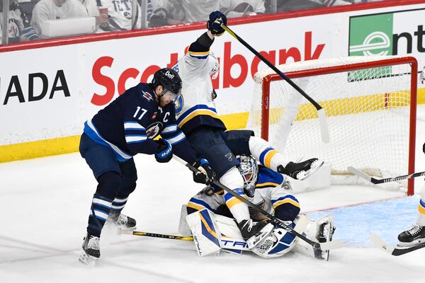 St. Louis Blues' Jake Neighbours, center, falls over Blues goaltender Jordan Binnington, right, as he is checked by Winnipeg Jets' Adam Lowry (17) during the third period of Game 2 of a first-round NHL hockey playoff series in Winnipeg, Manitoba, Monday April 21, 2025. (Fred Greenslade/The Canadian Press via AP)
