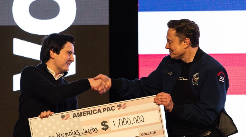 FILE - Elon Musk hands over a million dollar check to Nicholas Jacobs during a town hall in Green Bay, Wis., March 30, 2025. (AP Photo/Jeffrey Phelps, File)