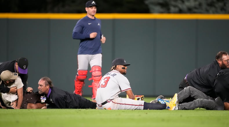 Ronald Acuna ends up on the turf as field guards wrestle down two fans who approached him as he took his spot in the field for the bottom of the seventh inning of a baseball game against the Colorado Rockies, Monday, Aug. 28, 2023, in Denver (AP Photo/David Zalubowski)