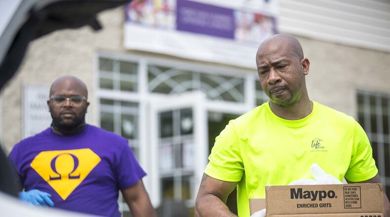 Elizabeth Baptist Church members Dimitri Yates (left) and Johnny Smith (right) give a family in need boxes of groceries and toiletries during an Atlanta Community Food Bank and Fulton County Schools collaborative distribution in Atlanta, Thursday, April 9, 2020. (ALYSSA POINTER / ALYSSA.POINTER@AJC.COM)