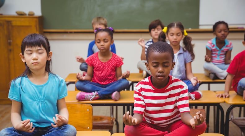 Pupils meditating in lotus position on desk in classroom. (Shutterstock)