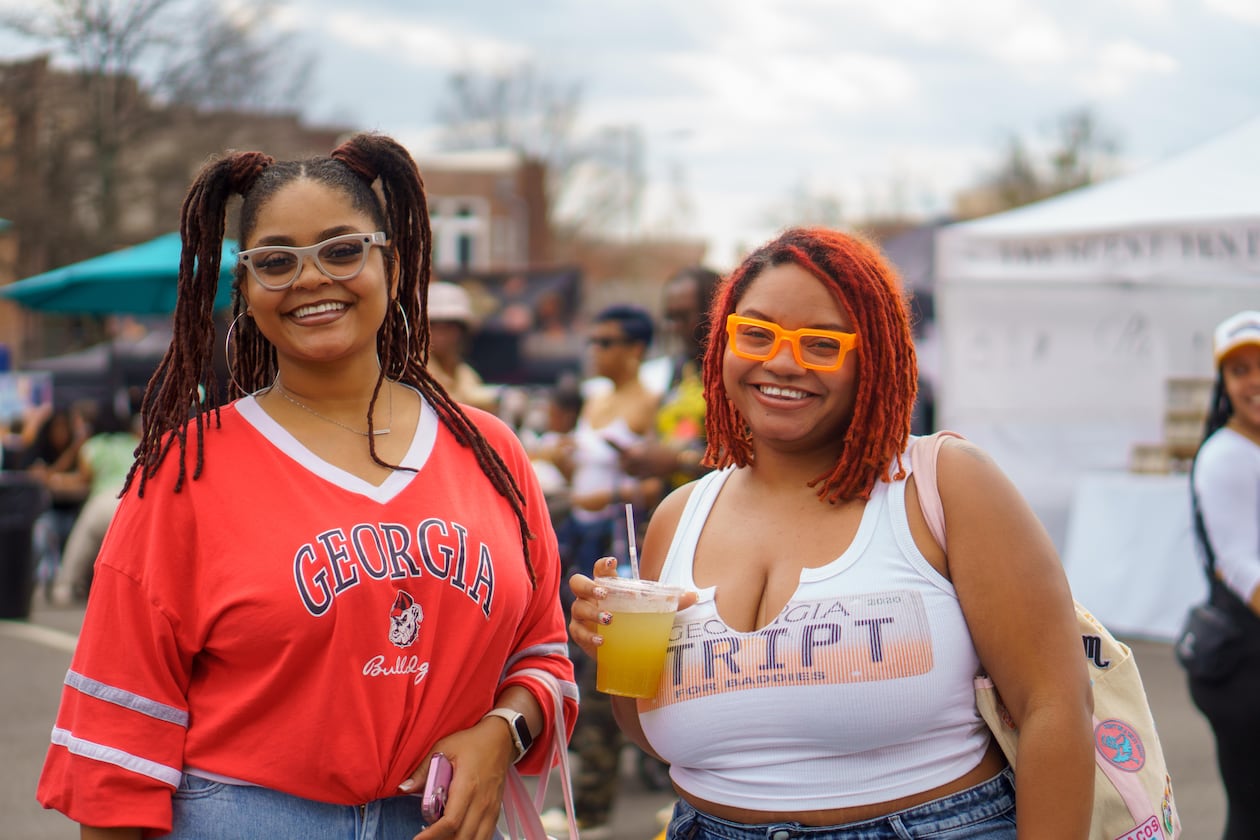 A woman in a red Georgia bulldogs t-shirt smiles next to another woman in a white Georgia tank top while she holds a drink at the Smorgasburg food festival.