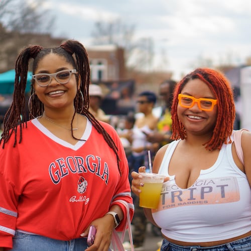 A woman in a red Georgia bulldogs t-shirt smiles next to another woman in a white Georgia tank top while she holds a drink at the Smorgasburg food festival.