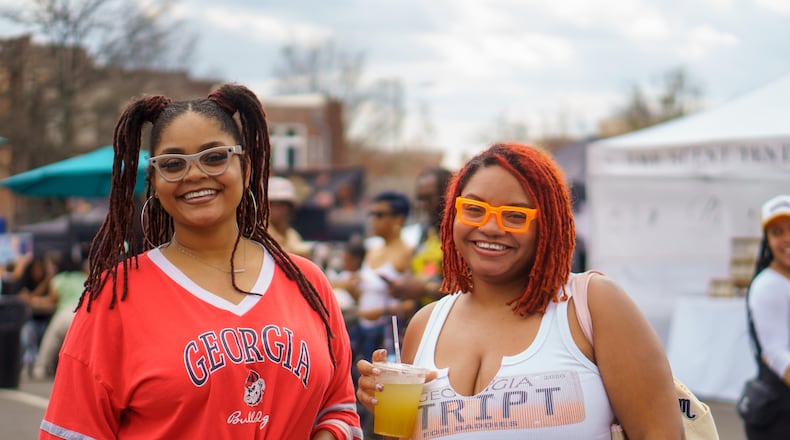 A woman in a red Georgia bulldogs t-shirt smiles next to another woman in a white Georgia tank top while she holds a drink at the Smorgasburg food festival.