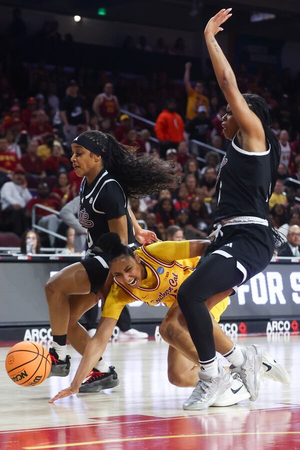 Southern California guard JuJu Watkins (12) falls to the floor with the ball between Mississippi State guard Eniya Russell, left, and guard Chandler Prater, right, during the first half in the second round of the NCAA college basketball tournament Monday, March 24, 2025, in Los Angeles. (AP Photo/Jessie Alcheh)