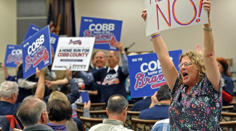 When I cover a town hall meeting or a public meeting, I try to go early. I often get a better picture before or after the meeting. I got this frame before the town hall meeting to get public input about the proposed Atlanta Braves stadium project. It visually told better story than the meeting itself. Made with a NIKON D3s camera, a 70-200 MM F 2.8 zoom lens set at 85MM, at F 4.5, a shutter speed of 1/200, and a ISO rating of 5000. November 21, 2013 Marietta - Elizabeth Reside, of Marietta, holding a sign to oppose new Atlanta Braves stadium as new stadium supporters rally (background) before a town hall meeting to get public input about the proposed Atlanta Braves stadium project at Cobb County Senior Wellness Center in Marietta on Wednesday, November 21, 2013. HYOSUB SHIN / HSHIN@AJC.COM