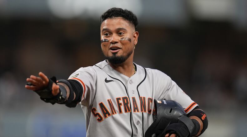 San Francisco Giants' Luis Arraez jokes with players in the San Diego Padres dugout as he stands on first base after getting hit by a pitch during the fourth inning of a baseball game Thursday, July 30, 2026, in San Diego. (AP Photo/Gregory Bull)