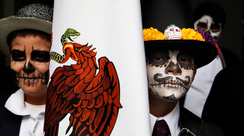 Children with their faces painted hold the Mexican national flag during a Day of the Dead celebration at a school in Mexico City, Monday, Oct. 31, 2016. The holiday honors the dead as friends and families gather in cemeteries to decorate their loved ones' graves and hold vigil through the night on Nov. 1 and 2. (AP Photo/Marco Ugarte)