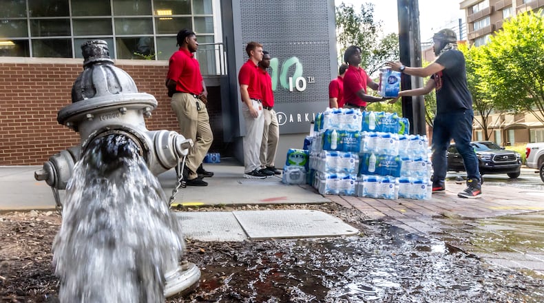 Atlanta Fire Rescue recruits (left) handed out water to Xaku Mitchell (right) on the corner of 10th Street and West Peachtree Street as crews worked Tuesday morning, June 4, 2024 at 11th and West Peachtree Street, one of two significant breaks since Friday afternoon that left thousands in the city with little or no pressure and many other residents forced to boil water. Businesses have also felt the impact and financial woes. (John Spink/AJC)
