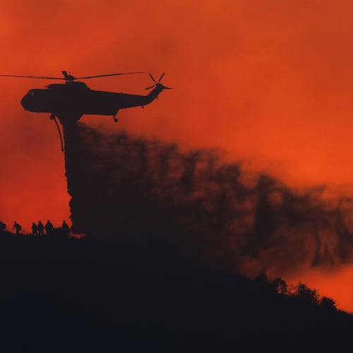 A water tanker drops water while firefighters walk below, as the Sandy Fire approaches, Tuesday, May 19, 2026, in Simi Valley, Calif. (AP Photo/Caroline Brehman)