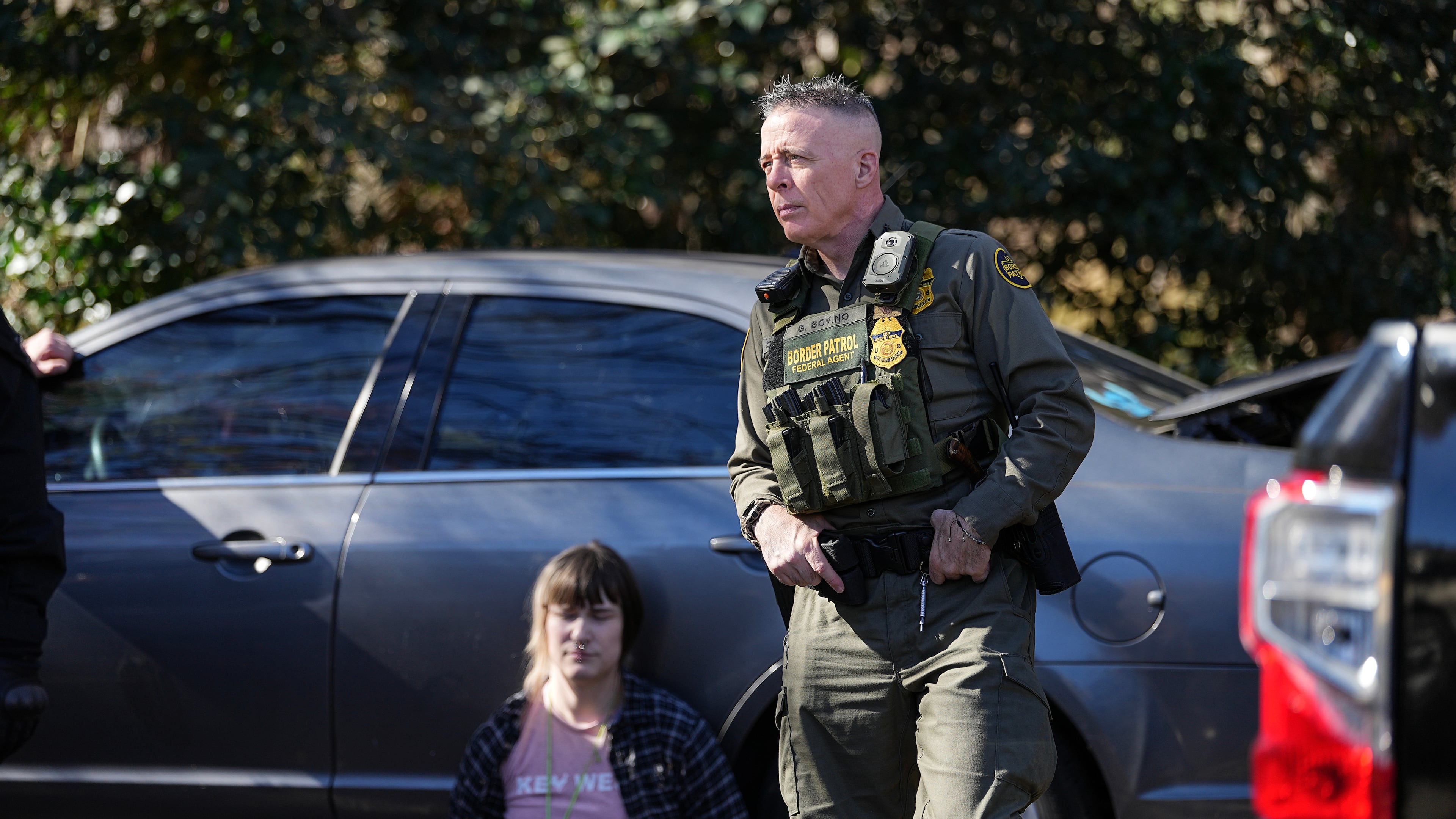 U.S. Border Patrol Commander at large Gregory Bovino, right, looks on as a detainee sits by a car, Monday, Nov. 17, 2025, in Charlotte, N.C. (AP Photo/Matt Kelley)