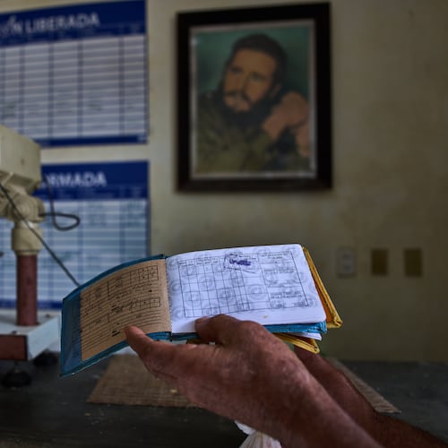 A man shows his ration book known as a "libreta," backdropped by a framed image of Fidel Castro, at a state-run bodega in Havana, Cuba, Saturday, May 2, 2026. (AP Photo/Ramon Espinosa)