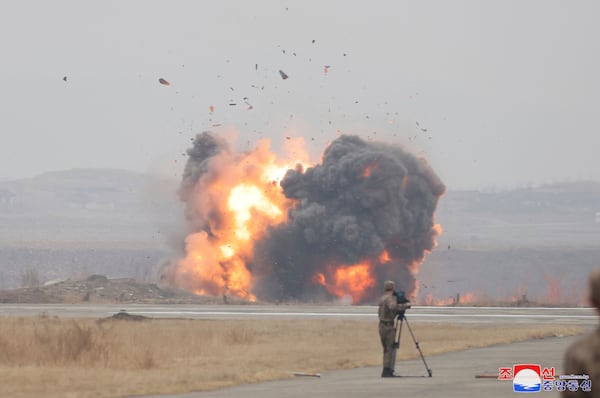 In this photo provided Thursday, March 27, 2025, by the North Korean government, a man in a military uniform films what is called an attack drone crashing into a prepared target at an undisclosed location in North Korea, earlier this week. Independent journalists were not given access to cover the event depicted in this image distributed by the North Korean government. The content of this image is as provided and cannot be independently verified. Korean language watermark on image as provided by source reads: "KCNA" which is the abbreviation for Korean Central News Agency. (Korean Central News Agency/Korea News Service via AP)