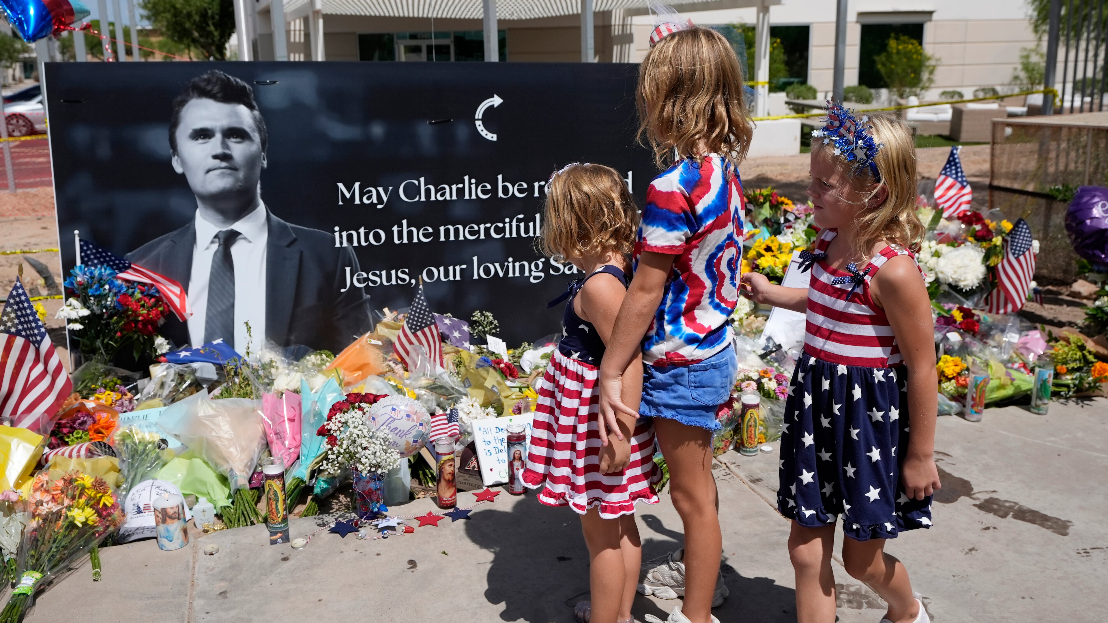 Sisters Clara Hetland, 4, left, Haddie Hetland, center, 9, and Audra Hetland 6, of Surprise, Ariz., spend time at a makeshift memorial set up at Turning Point USA headquarters after the shooting death at a Utah college on Wednesday of Charlie Kirk, the co-founder and CEO of the organization, Thursday, Sept. 11, 2025, in Phoenix. (AP Photo/Ross D. Franklin)