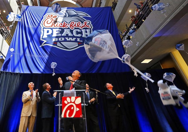 Steve Robinson (from left), Chick-fil-A executive vice president; Michael Kelly, College Football Playoff executive; Gary Stokan, bowl president; Rob Temple, ESPN vice president; and Burke Magnus, ESPN senior vice president, unveil the new Chick-fil-A Peach Bowl logo while parachuting cows drop from the ceiling in 2014. (AJC 2014) 