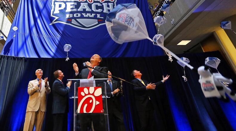 Steve Robinson (from left), Chick-fil-A executive vice president; Michael Kelly, College Football Playoff executive; Gary Stokan, bowl president; Rob Temple, ESPN vice president; and Burke Magnus, ESPN senior vice president, look up as the bowl’s new name Chick-fil-A Peach Bowl logo is unveiled while parachuting cows drop from the ceiling Monday, April 21, 2014, in Atlanta. CURTIS COMPTON / AJC file