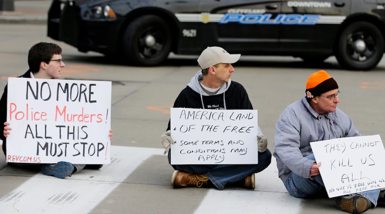 Three protesters block the road at Public Square Thursday, Dec. 4, 2014, in downtown Cleveland. The U.S. Justice Department and Cleveland reached an agreement Thursday to overhaul the city's police department after federal investigators concluded that officers use excessive and unnecessary force far too often and have endangered the public and their fellow officers with their recklessness.