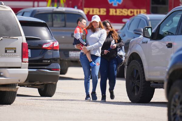 A woman carries a child as she and a student of Wilmer-Hutchins High School leave after authorities reported the campus had been secured following reports of a shooting, in Dallas, Tx., Tuesday, April 15, 2025. (AP Photo/Julio Cortez)