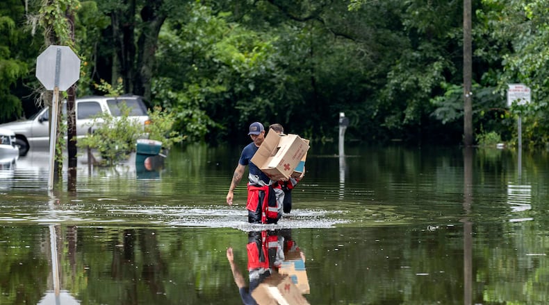 Savannah Fire Advanced Firefighters Andrew Stevenson, front, and Ron Strauss carry food to residents in the Tremont Park neighborhood that where stranded in flooding from Tropical Storm Debby, Tuesday, Aug. 6, 2024, in Savannah, Ga. (AP Photo/Stephen B. Morton)