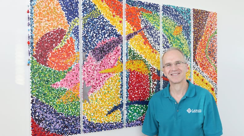 Dr. Scott Shulman poses for a portrait next to one of his pieces of art at the Laureate Medical Group in Atlanta. This piece is made from melted crayon. It is one of 38 pieces on display in four Laureate offices across the metro area. Shulman initially wanted to use his hands as a surgeon, but after deciding to go into internal medicine, he began using his hands to create art. EMILY HANEY / EMILY.HANEY@AJC.COM
