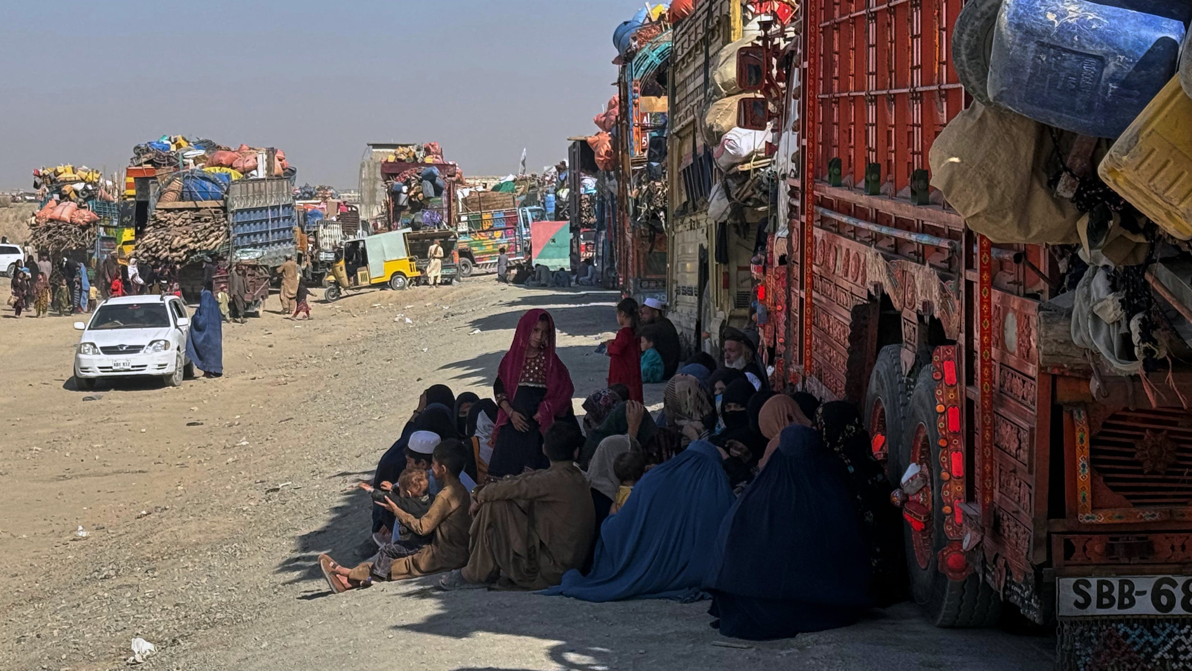 Afghan refugees sit beside trucks loaded with their belongings as they wait their turn to leave for their homeland through a border crossing point which partially opens following Oct.19 ceasefire on the outskirts of Chaman, a border town on the Pakistan Afghan border, Wednesday, Oct. 29, 2025. (AP Photo/H. Achakzai)